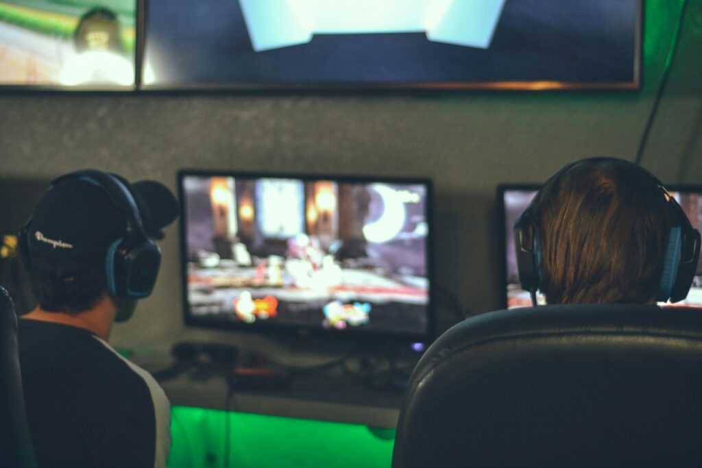 two persons playing video games in front of monitors two guys playing video games in front of monitors