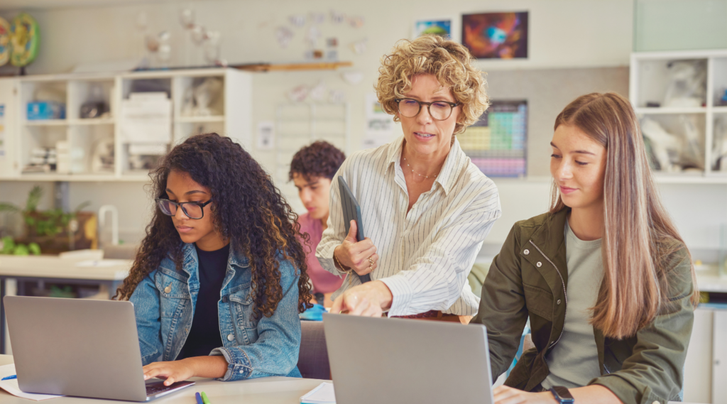 The teacher helps students with tasks on laptops in the classroom Teacher helps students with tasks on laptops in the classroom